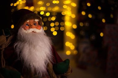 Noel Baba hediye dolu büyük bir çanta taşıyor, Noel ağacının yanında.