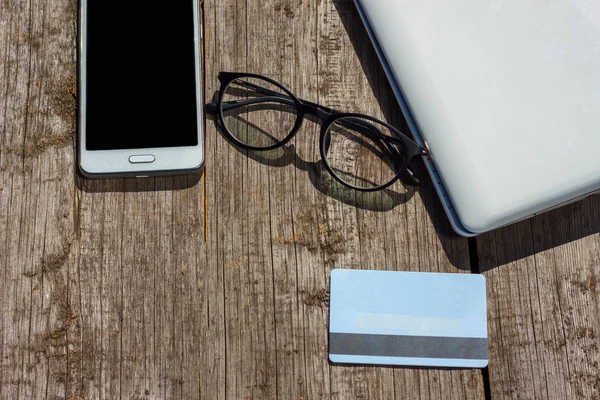 laptop phone glasses and credit card lie on wooden background