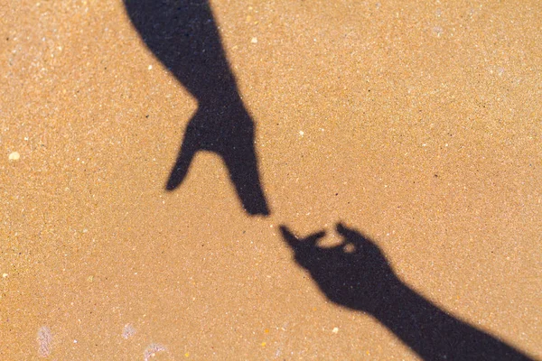 men\'s hand reaches for women\'s hand shadow on sand background