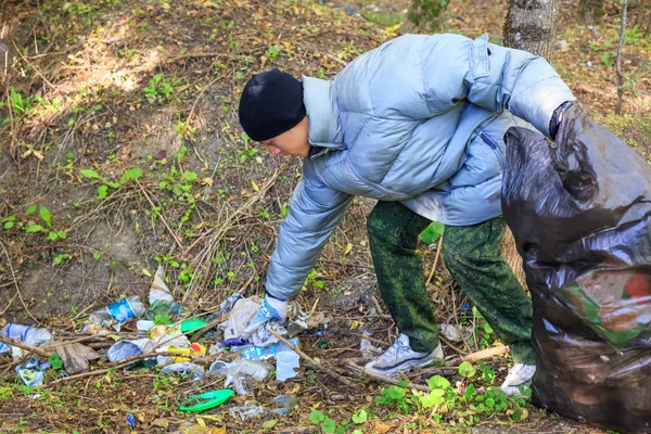 young man collects garbage in the forest