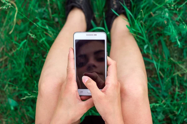 girl sitting with phone in hands on grass top view