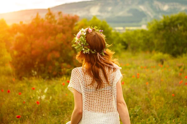 woman walking on a field of flowers at sunset with a wreath on his head.