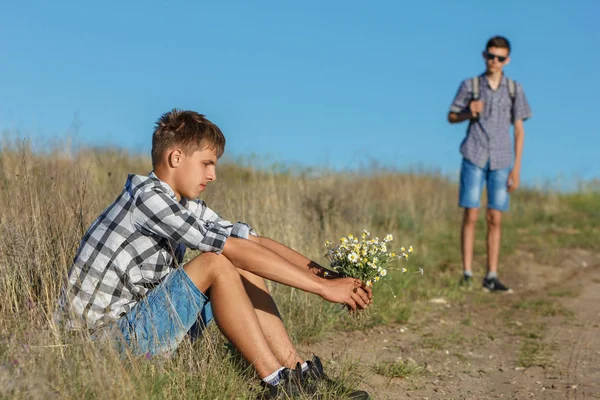 young man sitting by the road with flowers, waiting for another, the concept of relationship.