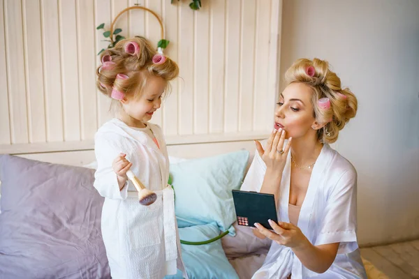 happy mom and daughter make a make-up sitting on the bed in the bedroom