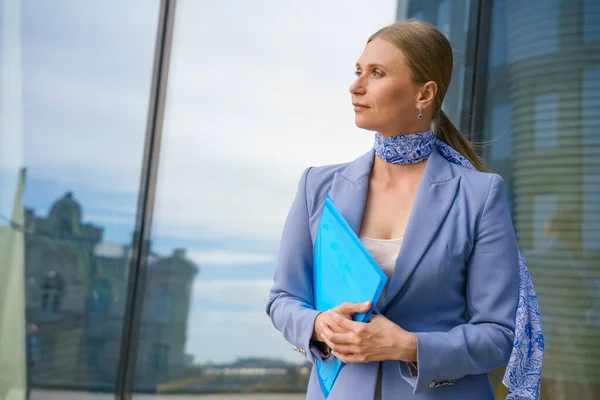 Business woman in suit with folder in her hand on background of business center