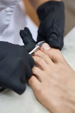 Siyah eldiven giyen bir uzman olarak profesyonel pedikür yapılıyor. Ayak bakımı için tırnak makaslarını dikkatlice kesiyor..