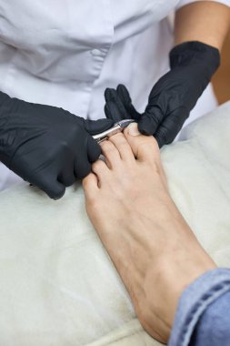 Profesyonel bir pediküre yakın durun. Siyah eldivenli bir uzman ayak tırnaklarını hijyen ve bakım makası ile dikkatlice kesiyor..