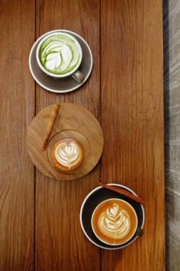 Bir fincan yeşil çay, matcha latte ve ahşap arka planda bir fincan sütlü kahve.