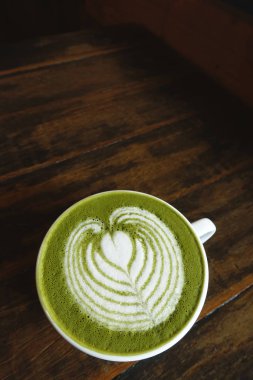Bir fincan yeşil çay, ahşap arka planda matcha latte.
