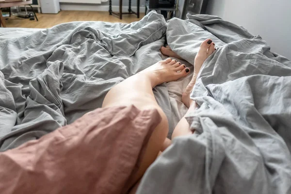 Men's and women's morning legs in bed under a blanket