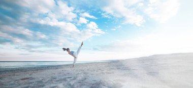 Genç kız gün batımında plajda yoga yapıyor.