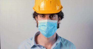 Kasklı bir adamın beyaz arka planda yüz maskesi takıp kameraya bakışının videosu. 