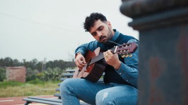 Adam bir bankta dinleniyor Gitarı açık havada çalıyor.