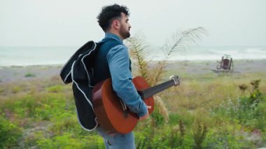 Gitarist, Deniz kenarında yürüyüş yaparak ilham arıyor.