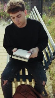 Adam parkta defterini kapatıp sırt çantasına koyuyor. . 