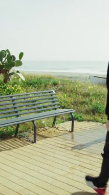 Üniversite öğrencisi okyanusun kenarındaki bir bankta dinleniyor. . 