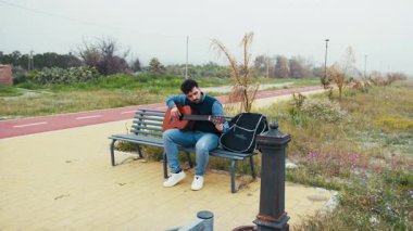 Adam bir bankta oturup gitar çalıyor..