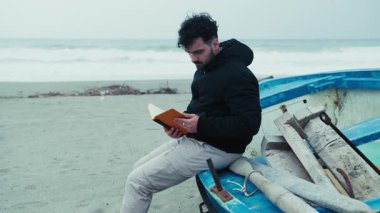 Kışın sahildeki adam teknede oturmuş notlarını okuyor.. 