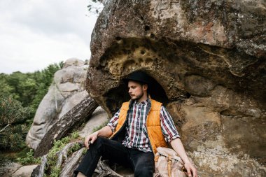 Genç bir erkek dağda zorlu bir tırmanıştan sonra bir kayanın yanında dinleniyor.