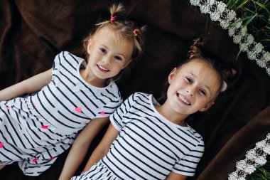 Üst Manzara. İki mutlu kız kardeş parkta kahverengi bir battaniyeye uzanıp kameraya bakıyorlar.