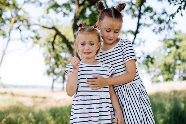 Little girl crying outdoors. The older sister takes care of her younger sister. Girlfriends