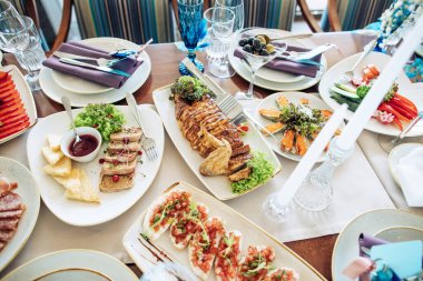 Tabaklarında yemek, dekor ve beyaz bir masa örtüsünde şamdanlar olan bir restoranda güzel bir düğün masası.