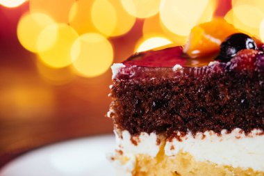 Bir parça kek krem çikolata meyve şekerli tatlı bokeh ışıklar ahşap ve kırmızı zemin üzerine ile