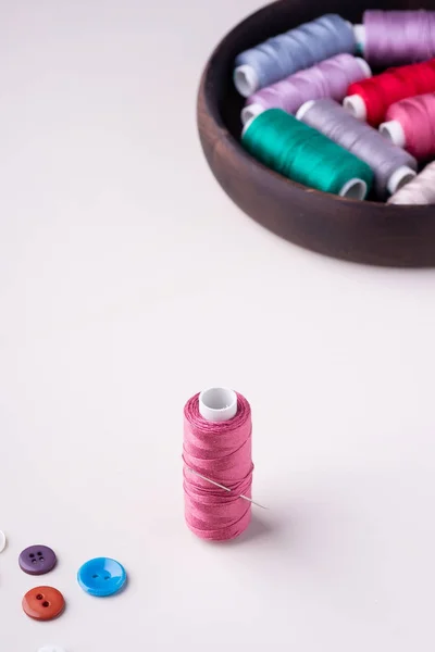 Angle view close up of pink thread coil with buttons and needle