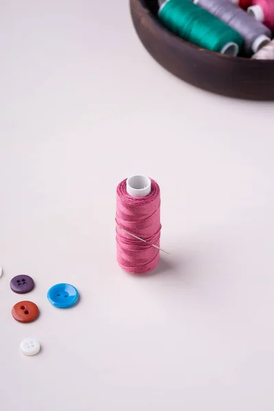 Angle view close up of pink thread coil with buttons and needle