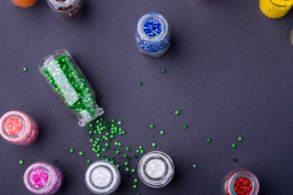 Scattered green beads from transparent bottle near varied colors beads dark background