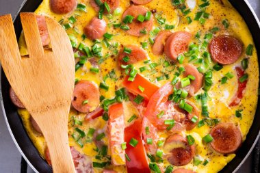 Ahşap spatula ile tavada domates, soğan ve sosis ile Omlet
