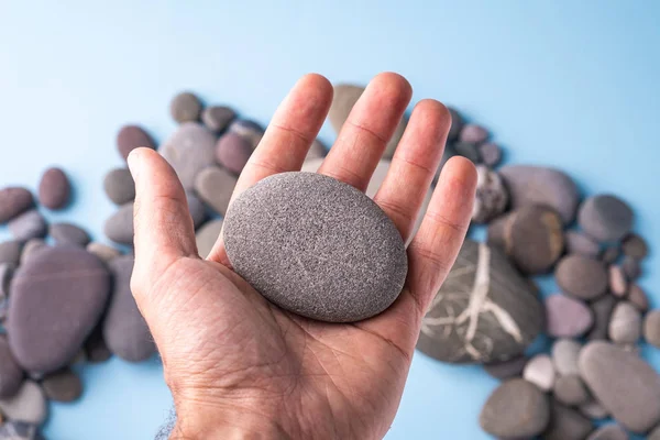 Pebble stone hold in hand on blue background with pebbles