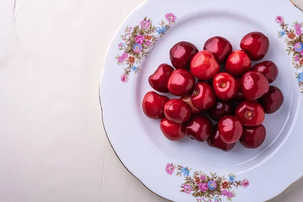 Cherry berries in white plate texture on wooden white background top view