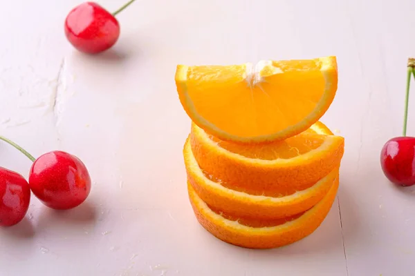 Summer fruit cherries with stacked oranges on white background angle view