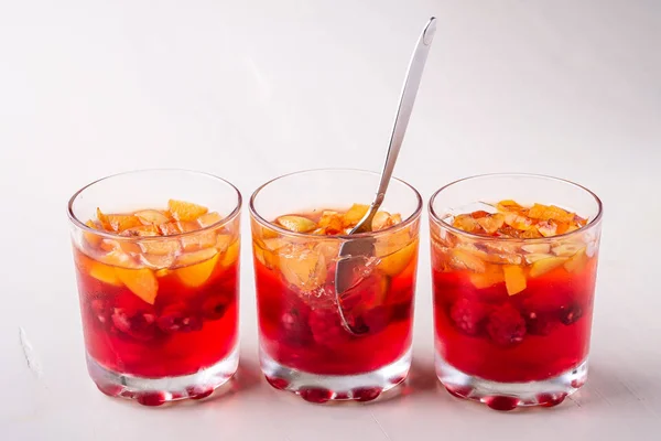 フルーツアプリコットラズベリーと一緒にシングルスプーン黄色の赤い夏の白い背景を持つ3つの飲み物のグラスでゼリーデザート — ストック写真