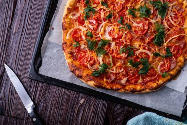 Taze pişmiş sıcak pizza peynir jambon et domates soğan maydanoz ev yapımı parşömen kağıt üzerine mutfak bıçağı ile fırın levha tepsisi tarifi koyu ahşap masa