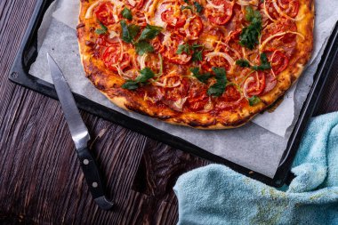 Taze pişmiş sıcak pizza peynir jambon et domates soğan maydanoz ev yapımı parşömen kağıt üzerine mutfak bıçağı ile fırın levha tepsisi tarifi koyu ahşap masa