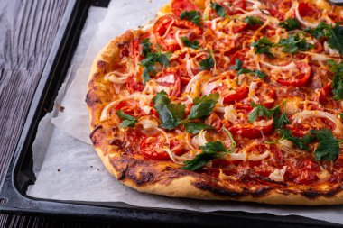 Taze pişmiş sıcak pizza peynir jambon et domates soğan maydanoz ev yapımı parşömen kağıt üzerinde fırın levha tepsi tarifi koyu ahşap masa