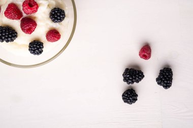 Beyaz ahşap arka plan üzerinde dağınık yığın meyveleri ile yakın cam kase böğürtlen ve ahududu ile İrmik puding yulaf püresi, Kahvaltı, izole, üst görünüm