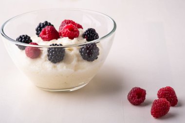 Beyaz ahşap arka plan üzerinde dağınık yığın çilek ile yakın cam kase böğürtlen ve ahududu ile İrmik puding lapası tatlı, Kahvaltı, izole