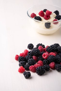 Beyaz ahşap arka plan üzerinde dağınık yığın çilek ile yakın cam kase böğürtlen ve ahududu ile İrmik puding lapası tatlı, Kahvaltı, izole