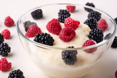 Beyaz ahşap arka plan, Kahvaltı, izole, seçici odak üzerinde sipariş çilek dağınık yığını ile yakın cam kase böğürtlen ve ahududu ile İrmik puding yulaf püresi