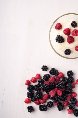 Beyaz ahşap arka plan üzerinde dağınık yığın meyveleri ile yakın cam kase böğürtlen ve ahududu ile İrmik puding yulaf püresi, Kahvaltı, izole, üst görünüm