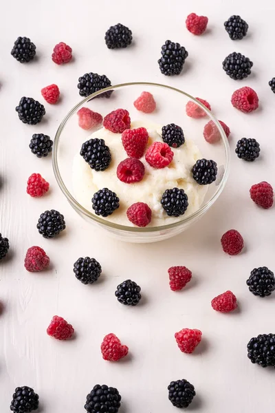 Beyaz ahşap arka plan, Kahvaltı, izole, seçici odak üzerinde sipariş çilek dağınık yığını ile yakın cam kase böğürtlen ve ahududu ile İrmik puding yulaf püresi