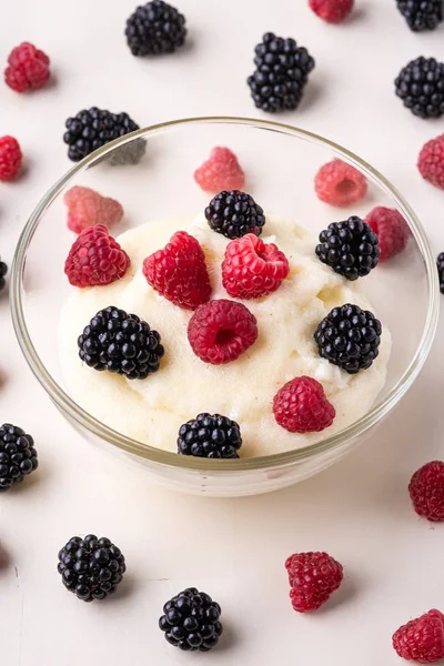 Semolina pudding porridge dessert with blackberry and raspberry in glass bowl near with scattered heap in order berries on white wooden background, breakfast, isolated, selective focus