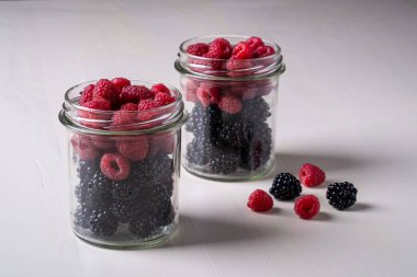 Beyaz ahşap masa arka plan üzerinde iki cam kavanoz ahududu ve böğürtlen tatlı organik sulu çilek