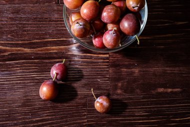 Koyu karamsar ahşap masa arka plan, sert ışık, kopya alanı üzerinde dağınık erik ile yakın cam kase olgun tatlı erik meyve