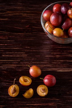 Koyu karamsar ahşap masa arka plan üzerinde dağınık dilimlenmiş yarım erik yakın cam kase su damlaları ile olgun tatlı erik meyve