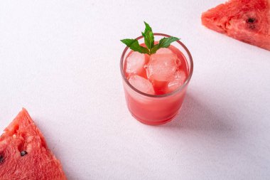 Beyaz arka planda iki dilim karpuz, fotokopi alanı, açı görünümü, seçici odak cam içecek buz küpleri ve yeşil nane yaprağı ile taze soğuk karpuz suyu