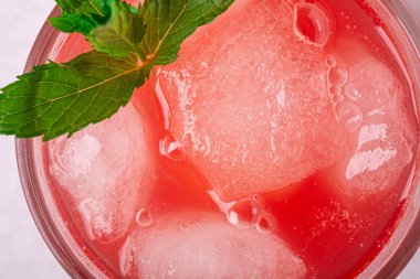 Beyaz arka plan, makro, seçici odak cam içecek buz küpleri ve yeşil nane yaprağı ile taze soğuk karpuz suyu
